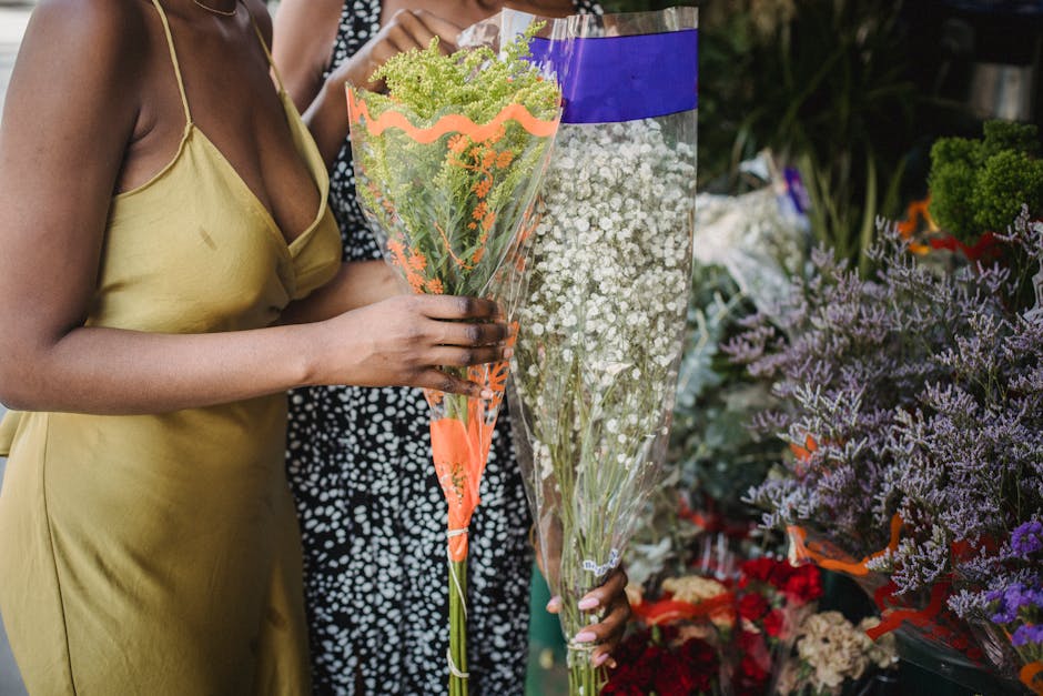 A woman dressed in a yellow camisole holds a bouquet of mixed flowers wrapped in transparent plastic with orange and purple accents. The bouquet features a variety of green and white blooms, including