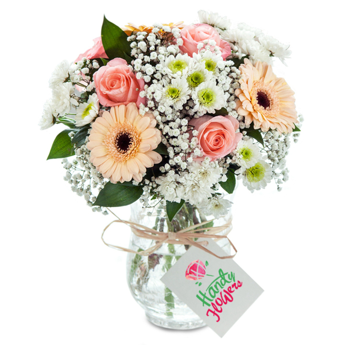 Radiating warmth and sophistication, this artful bouquet graces a pristine setting reminiscent of the welcoming homes and studios scattered through Forest Hill. At its core, majestic peach-pink roses with lush, velvety petals capture timeless affection, offering a soft, fragrant focal point that recalls leisurely walks beneath forest canopies. Vibrant peach gerbera daisies, each defined by a dark chocolatey center, provide bright, joyful accents that feel as bold as the murals along Grierson Road. Sprigs of supple white baby's breath infuse the arrangement with a light, cloud-like texture, their tiny blossoms casting delicate shadows that soften the overall composition. Interwoven with these are plump white chrysanthemums tinged with lively lime green centers, echoing the new growth of spring found in local allotments. Lush eucalyptus leaves, mottled dark and silvery, surface throughout for grounding contrast and a gentle woodland fragrance. The bouquet is securely nestled in a clear, textured glass vase that amplifies the interplay of submerged green stems and sparkling water, a quiet nod to the fresh quality of Forest Hill flowers. Wrapping the neck of the vase, a length of rustic twine is tied into an easy knot, securing a classic white rectangular tag-a blank slate for heartfelt messages. This bouquet, prepared by local hands, is perfect for commemorating life's special milestones or simply adding an elegant flourish to Forest Hill gatherings.