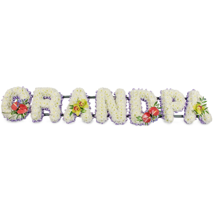 The photograph captures a refined, personalised funeral tribute that spells out GRANDPA in a linear row of large block capitals, all set against a plain white backdrop that allows the floristry work to stand out clearly. Each letter is carefully constructed and then densely covered with pristine white chrysanthemums, their round, petal-rich heads positioned side by side until the structure beneath disappears and only a soft, even blanket of white remains. This uniform texture suggests serenity and purity, a fitting symbol for a final tribute to a grandfather. Along the base of every letter, a slim edging of pale lavender ribbon can be seen, running like a continuous lilac thread beneath the flowers, helping to define the silhouettes and introducing a quiet hint of colour. Behind the word, a dark green bar connects all the letters, providing practical support so the tribute can be displayed with confidence at a funeral in Forest Hill, perhaps resting on trestles inside a chapel or at a graveside among the mature trees the area is known for. Carefully placed bursts of richer shade add both balance and emotional depth: the G on the left and the D nearer the centre each carry a compact arrangement of deep red anthuriums, their glossy, heart-shaped forms and central spadices rising from a bed of dark green leaves and subtle filler blooms. On the first A and the final A at the far right, sprays of yellow-green orchids bring a lighter, contemporary feel, the delicate flowers and fresh lime tones standing out gently against the white chrysanthemum base. Overall, the piece feels crafted and considered, an eloquent floral statement for families in Forest Hill wishing to honour a beloved grandpa with grace and respect.