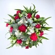 Viewed from above against a pristine white background, this abundant round bouquet appears almost like a colourful garden gathered into two hands. Deep crimson red roses sit at the heart of the design, some still cupped in tight buds, others beginning to unfurl soft, velvety petals that suggest romance and tenderness. Around them, ruffled carnations in rich fuchsia and ruby tones add energy and movement, their many layers catching the light and creating a sense of festive texture. Clusters of small, daisy-like white spray chrysanthemums bring brightness and clarity, their clean, simple faces lifting the whole arrangement in the same way a sunny morning brightens the streets around Forest Hill station. Threaded between the larger blooms are airy sprigs of white gypsophila, or baby's breath, forming a delicate cloud that softens the stronger colours and gives the bouquet a gentle, almost misty glow. Luxurious greenery holds everything together: broad, pointed leaves, likely from lilies or alstroemeria, radiate outward to give structure, while round, silvery eucalyptus leaves nestle between flowers, their cool, muted green lending a modern touch you might see in a stylish home just off London Road. The foliage feels fresh and crisp, as though it has just been conditioned in a busy local workshop, ready for same-day delivery across Forest Hill and the nearby streets that slope down towards Dulwich. The overall mood is joyful yet elegant, perfect for sending love, warm congratulations, or a heartfelt get-well wish, with every petal and leaf arranged to create a full, generous impression of care and celebration.