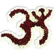 A serene, reverent floral sculpture of the sacred Om (Aum) symbol sits against a pure white backdrop, painstakingly formed from thousands of small, densely packed deep maroon-red chrysanthemum-like blooms. Each rich red pompon carries a tiny lime-green eye at its centre, a subtle natural contrast that makes the mass of petals read as a warm, living texture when seen up close. The symbol's familiar '3'-like curve, the sweeping downward stroke and the small crescent-and-dot above are crisply modelled, their negative spaces traced and defined by a generous, undulating border of pristine white spray chrysanthemums. That white outline gives the whole piece a luminous halo, lifting the dark interior and making the calligraphic shape read clearly even from a distance. The arrangement is sculptural and lush, petals layered so tightly they form a velvety surface; a soft drop shadow beneath suggests three-dimensional presence on the white field. In quiet light the flowers would feel cool and slightly dewy to the touch, their fragrance faintly earthy and consoling-an appropriate companion for meditation, devotional ceremony, or a respectful memorial. The workmanship speaks of patient, practiced hands arranging each bloom to maintain the symbol's sacred balance and rhythmic curves. Thoughtfully composed for use in spiritual gatherings, yoga events, or cultural observances near Forest Hill's Horniman Museum gardens and Dartmouth Road, this piece communicates deep reverence and visual clarity while remaining grounded in natural texture and scent.